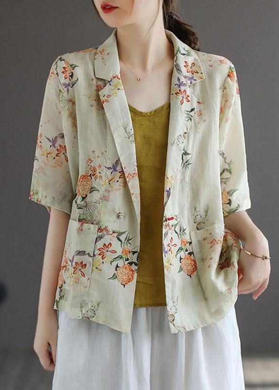 Woman wearing a floral print jacket over a yellow top and white pants on a gray background