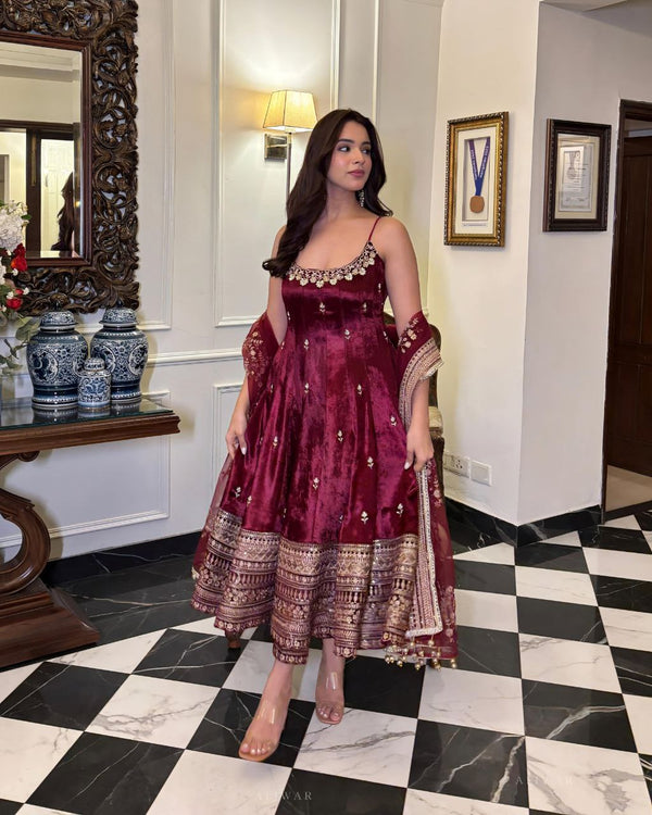 Woman in a maroon traditional dress standing in a room with checkered floor and decorative items.