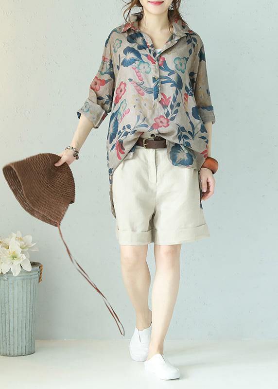 Woman wearing a floral blouse and beige shorts with a plain background