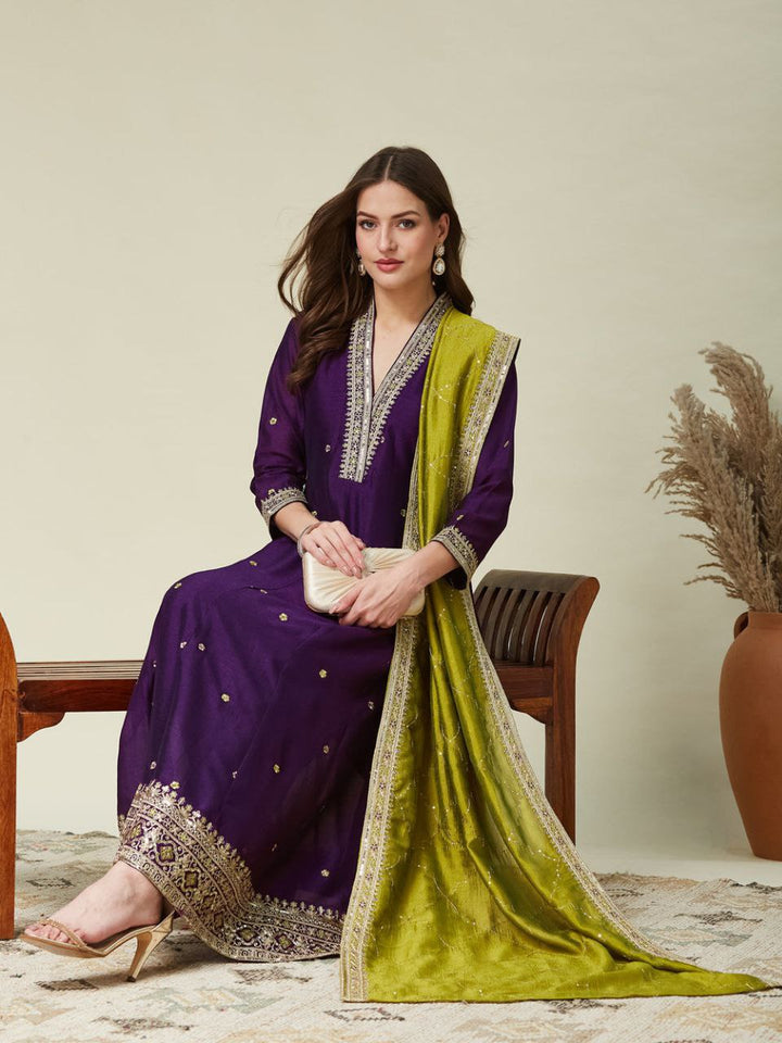 Woman wearing a purple Roman Silk Anarkali outfit with zari embroidery and green dupatta.
