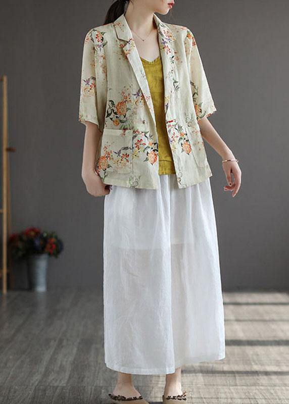 Woman wearing a floral kimono-style jacket over a yellow top and white skirt in a minimal setting.