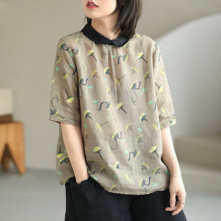 Person wearing a light brown blouse with floral patterns and black collar in a minimal indoor setting.