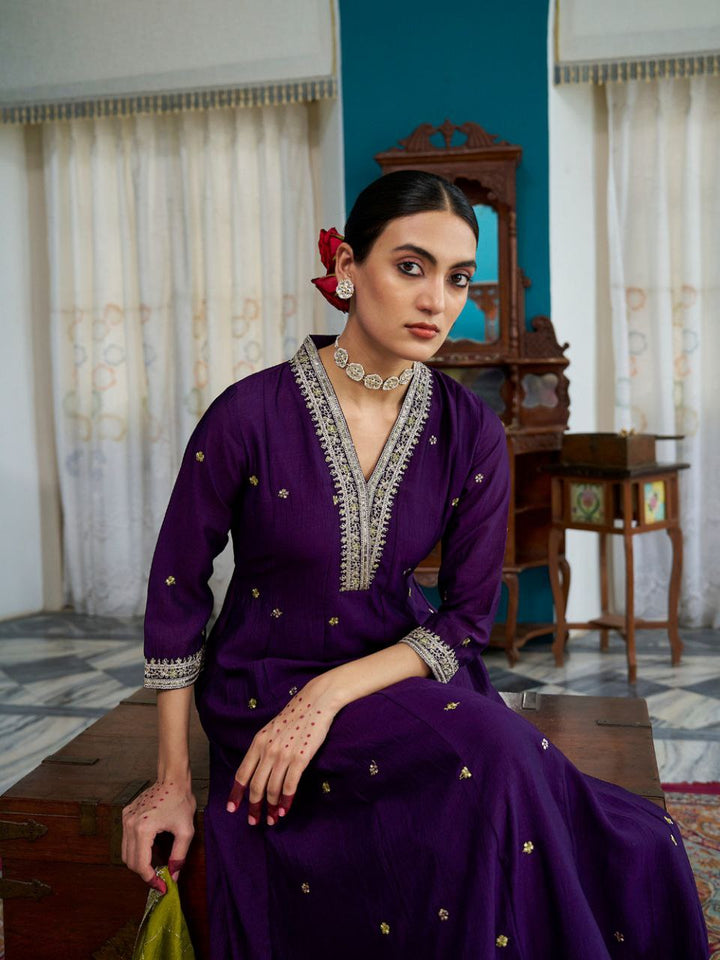 Woman in a purple traditional outfit with gold embroidery sitting on a wooden bench.