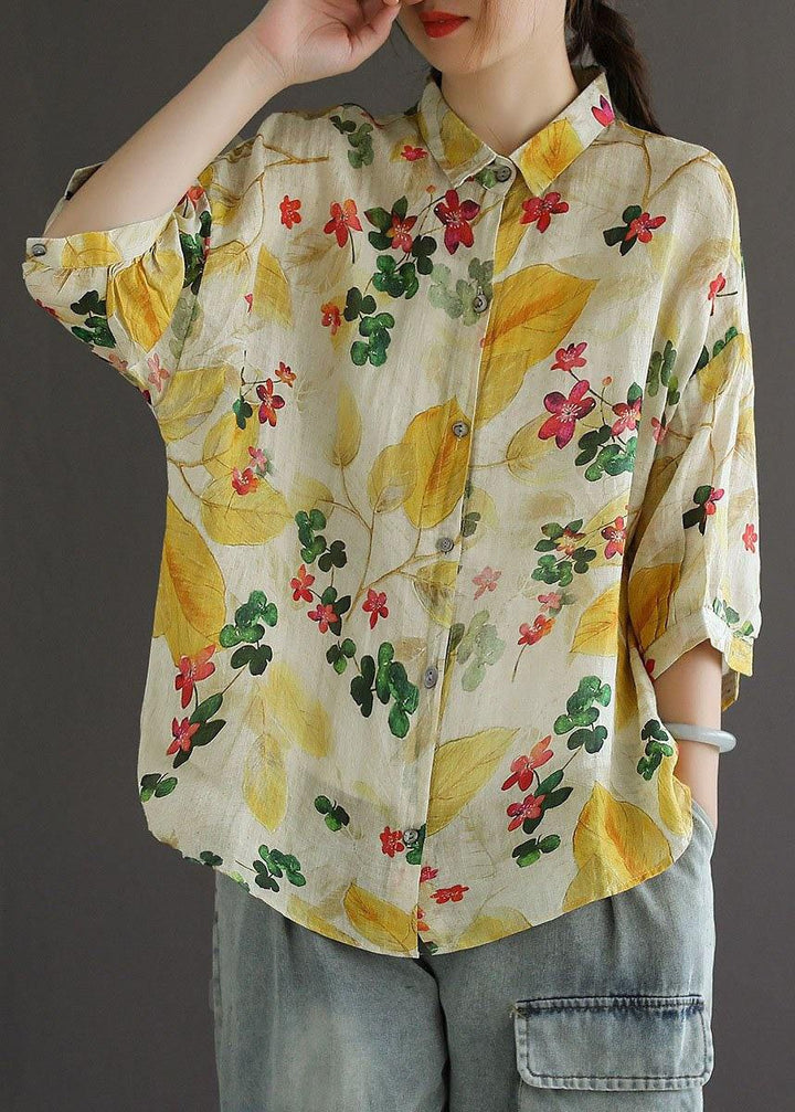 Person wearing a floral shirt with yellow leaves and red flowers on a plain background