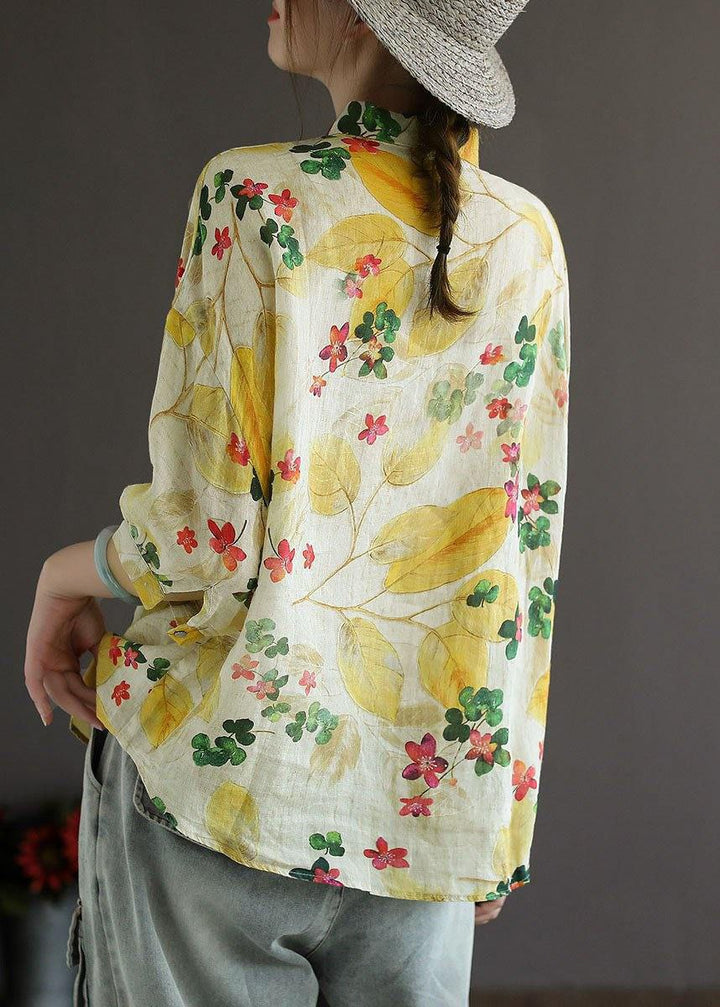 Person wearing a floral-patterned shirt with yellow leaves and flowers on a plain background
