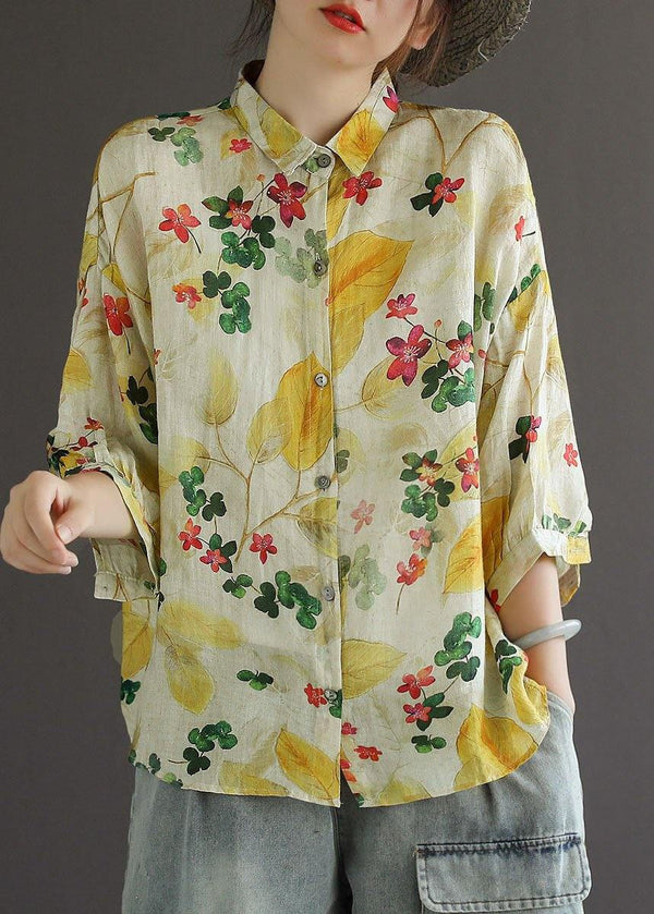 Person wearing a floral blouse with yellow and red flowers on a plain background