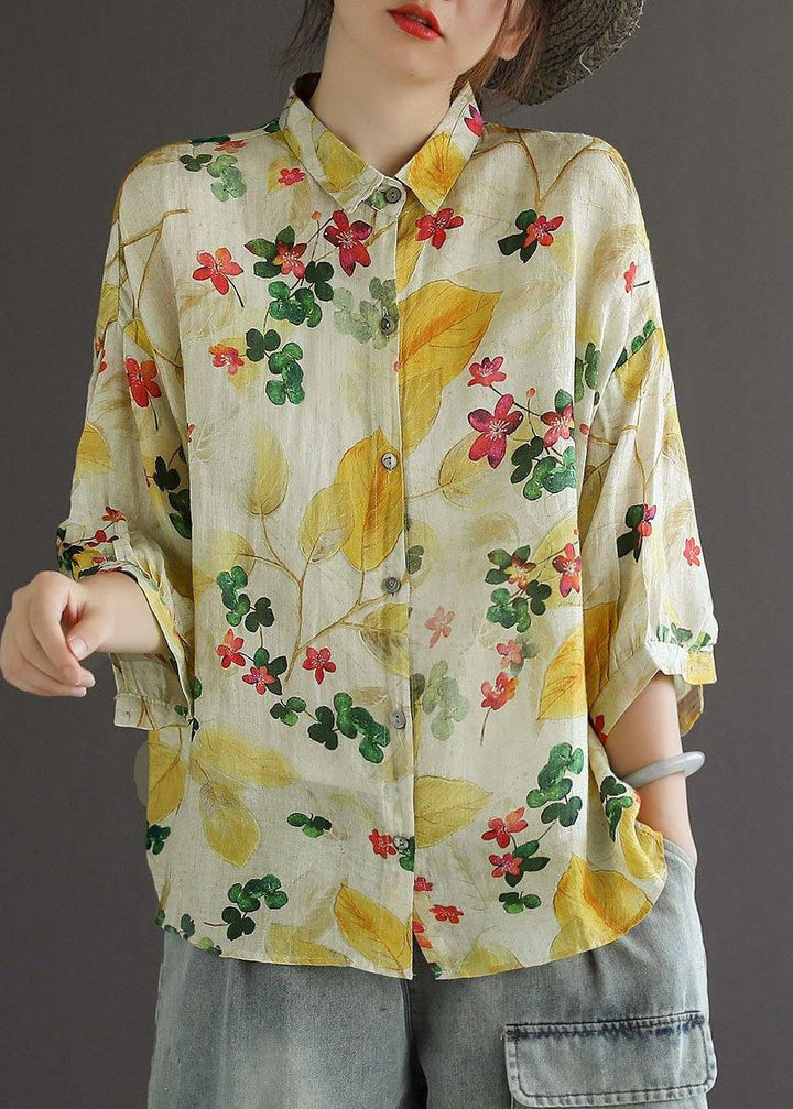 Person wearing a floral blouse with yellow and red flowers on a plain background